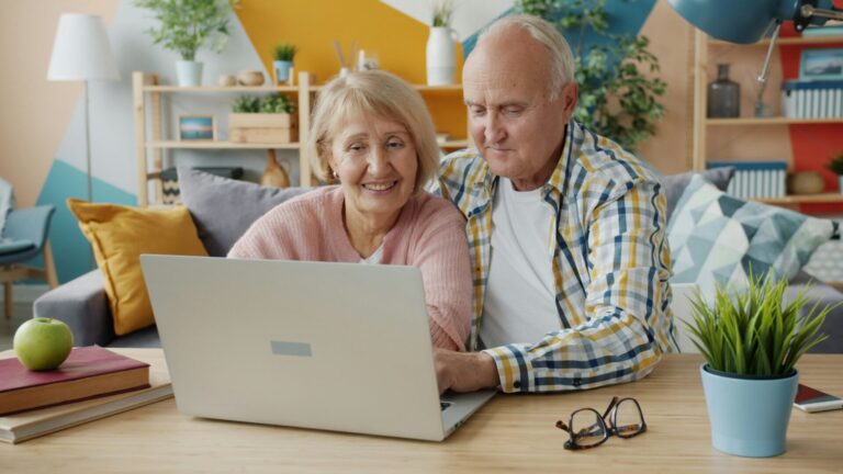 Älteres Paar sitzt gemeinsam vor einem Laptop am Tisch